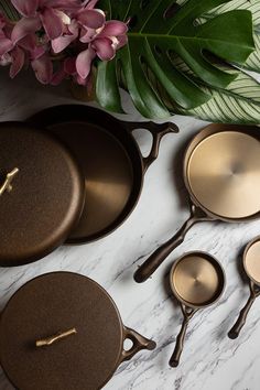 three pots and two pans on a marble counter top with flowers in the background