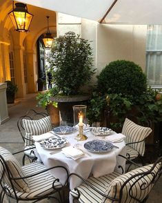 an outdoor dining area with white table cloths and blue plates on it, surrounded by potted plants