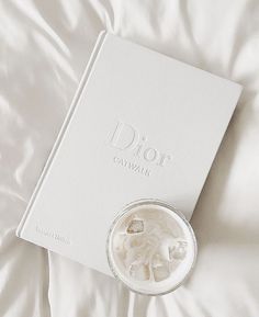 a white book sitting on top of a bed next to a glass filled with liquid