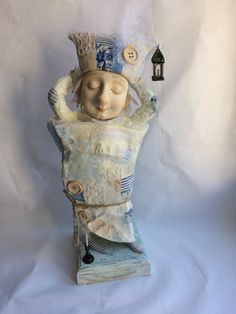 a ceramic sculpture of a woman wearing a hat and holding her arms in the air