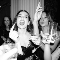 black and white photograph of people at a party with drinks in their hands, one woman holding up her hand