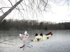 two stuffed animals sitting on top of snow covered ground next to a frozen lake with trees in the background