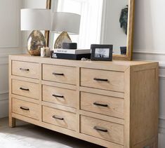 a wooden dresser sitting next to a large mirror and lamp on top of it's sideboard