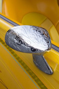 a shiny chrome door handle on a yellow car with an intricate design in the center