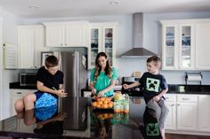 three children are sitting on the kitchen counter and one boy is standing in front of the refrigerator