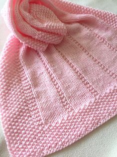 a pink knitted scarf laying on top of a bed