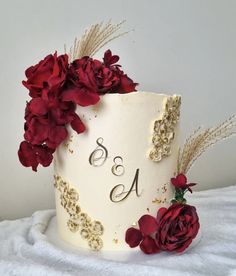 a wedding cake decorated with red flowers and gold glitters is displayed on a white tablecloth