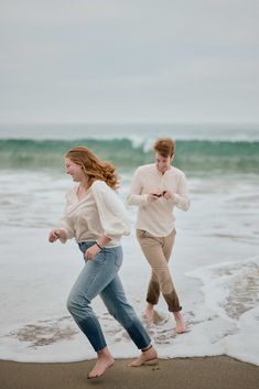 two people are running on the beach in front of the ocean and one person is using a cell phone
