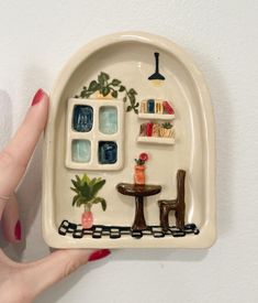 a hand holding a ceramic plate with miniature furniture on it