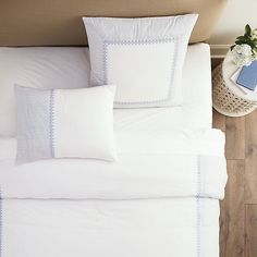 a bed with white sheets and blue trimmings on the headboard is shown