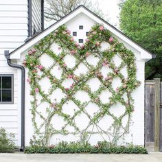 a white building with pink flowers growing on it's side and a wooden fence behind it