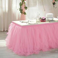 a table with a pink tulle skirt on it and flowers hanging from the ceiling