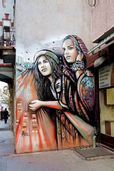 a painting on the side of a building with two women hugging each other and birds flying overhead