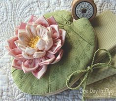 there is a small flower on top of a green heart shaped pillow with a clock in the middle