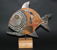 a metal fish sculpture sitting on top of a wooden block next to a black wall