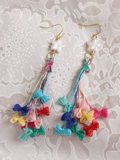 two pairs of colorful tasselled earrings on top of a white lace tablecloth