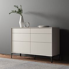 a white dresser sitting on top of a wooden floor next to a vase and bowl