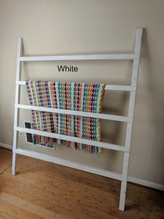 a white shelf with a multicolored blanket hanging on it's side next to a wooden floor