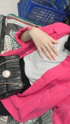 a doll is laying down with a purse on it's lap and wearing a pink jacket