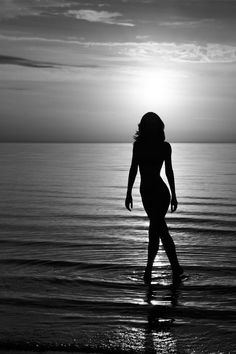 a woman standing on top of a beach next to the ocean under a cloudy sky