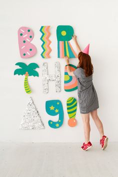 a woman standing in front of a wall decorated with letters and palm trees, wearing a party hat