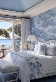 a bedroom with blue and white wallpaper has a large window overlooking the water in front of it