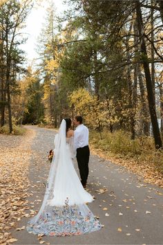 a bride and groom standing on a path in the woods with leaves all around them