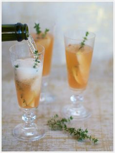 two glasses filled with champagne and garnished with herbs, one being poured into the glass