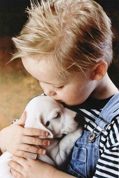 a young boy holding a white puppy in his arms and kissing it's face