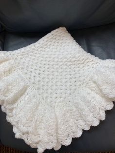 a white crocheted blanket sitting on top of a black leather chair next to a pillow