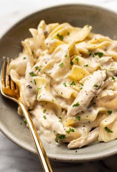 a pasta dish with chicken and cream sauce in a bowl next to a gold fork