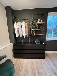 an empty room with clothes hanging on the wall and a green chair in front of it