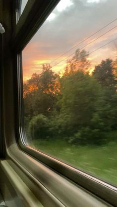 the sun is setting over some trees and grass from inside a train window, as seen from outside