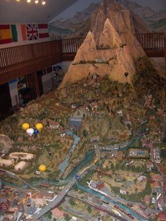 a model train set is shown on display in a museum with mountains and flags hanging from the ceiling