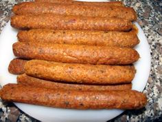 several sausages on a white plate sitting on a granite counter top