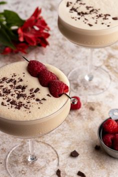 two glasses filled with dessert and raspberries on a table