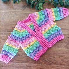 two crocheted mittens sitting on top of a wooden table next to green leaves