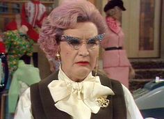 an older woman with pink hair wearing glasses and a bow tie