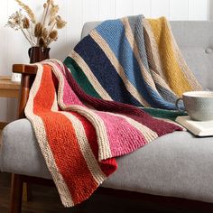 a couch with a blanket on top of it and a cup next to the couch