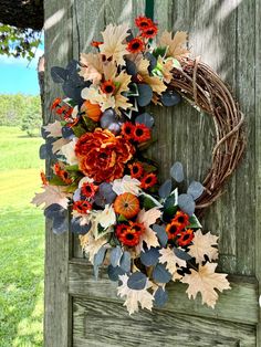 a wreath is hanging on the side of a wooden door with leaves and flowers around it