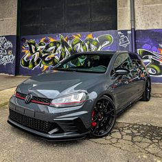 a grey car parked in front of a graffiti covered building with black rims and red brake pads
