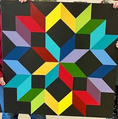 two people holding up a large piece of art made out of different colored paper squares