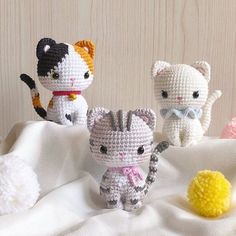 three crocheted kittens sitting on top of a white blanket next to a yellow ball