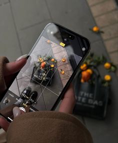 a person holding an iphone in their hand with oranges on the table behind them