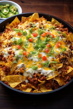 a skillet filled with nachos and cheese on top of a wooden table