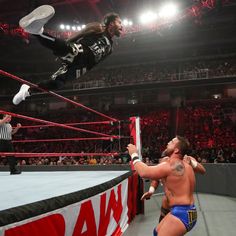 two wrestlers in the middle of a wrestling match, one is jumping over the ring