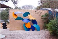 a sculpture in front of a building with trees and bushes around it on the ground