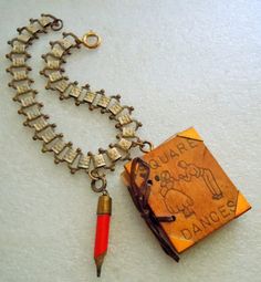 a necklace with an old book and a red pen on the chain that is attached to it