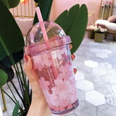 a person holding a pink drink with flowers on it and a straw in their hand