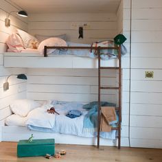 two bunk beds in a room with white walls and wood flooring, along with a green suitcase